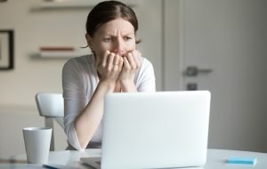 Portrait of a young woman at desk with laptop, fear